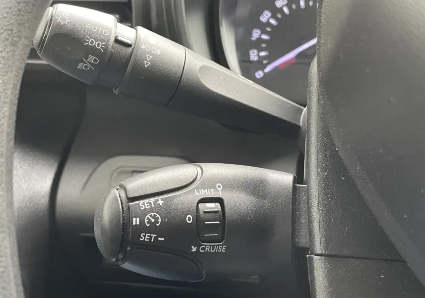 Gros plan sur la commande de régulateur de vitesse noire à gauche du volant dans l'habitacle du Citroën Berlingo blanc 2018.