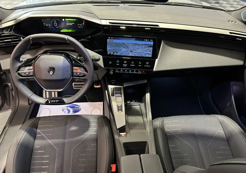 Vue intérieure avant de la Peugeot 308 GT 2026, tableau de bord numérique et écran tactile central avec finition noire élégante.