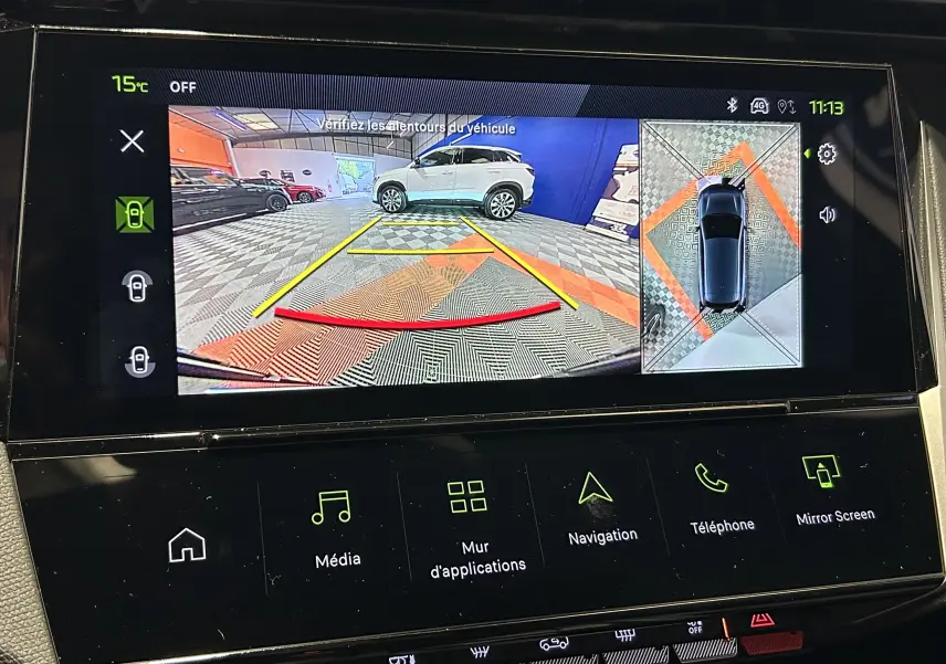 Vue écran intérieur du système Vision 360° montrant une voiture blanche en vue arrière avec lignes de guidage colorées.