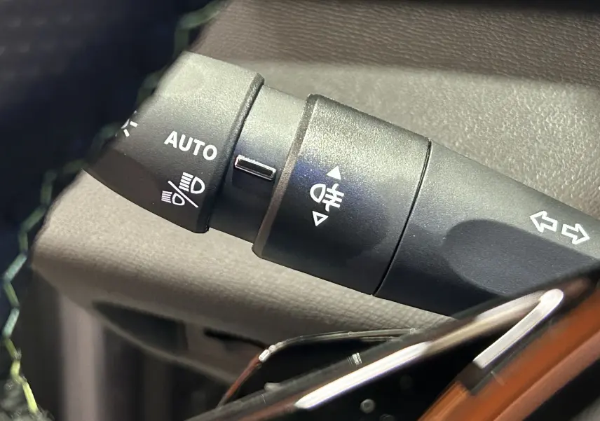Gros plan sur la commande de phares automatique et clignotants du Peugeot 308 GT Gris Artense, intérieur sombre.