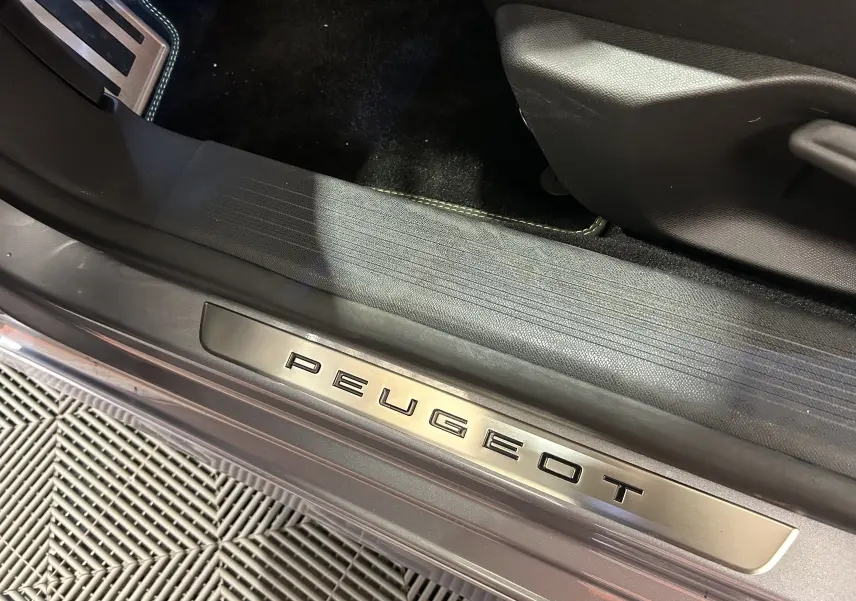 Gros plan sur la plaque de seuil de porte Peugeot en métal brossé, intérieur noir et extérieur gris Artense visible.