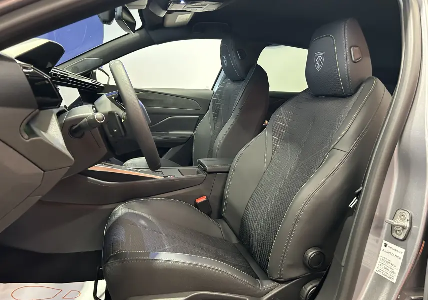 Vue intérieure côté conducteur de la Peugeot 308 GT gris Artense, sièges noirs avec logo Peugeot brodé sur les appuie-têtes.