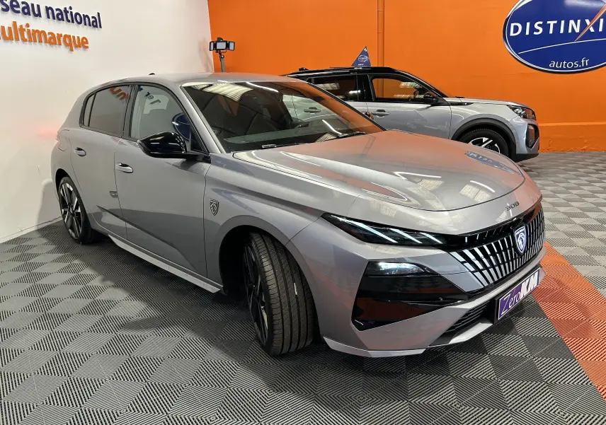 Peugeot 308 gris Artense vue 3/4 avant droit, avec calandre distinctive et jantes noires en intérieur showroom.