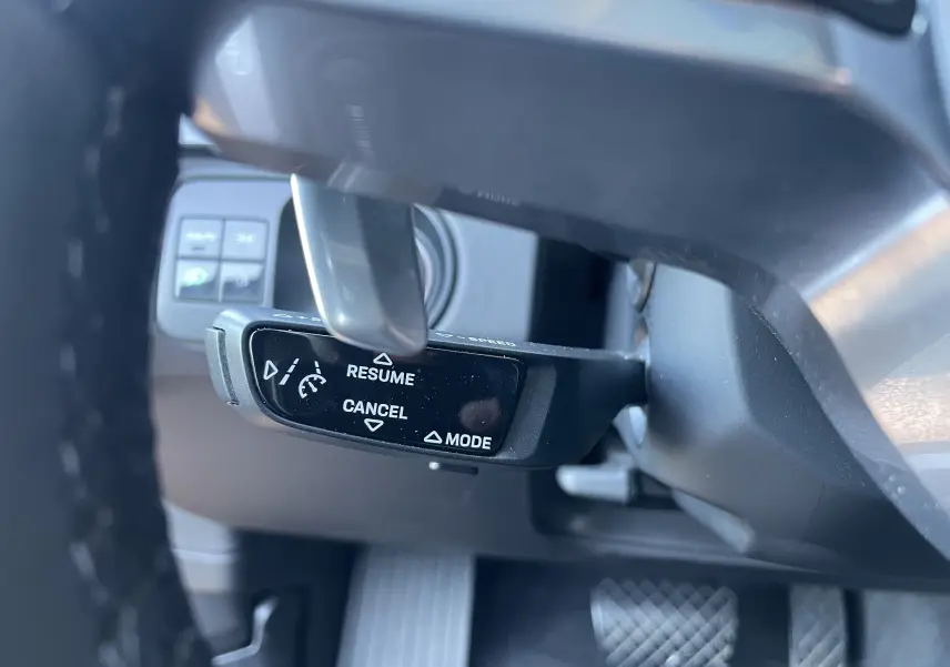 Gros plan sur la commande de régulateur de vitesse au volant d’un Porsche Cayenne Coupé E-Hybrid noir, intérieur gris/noir.