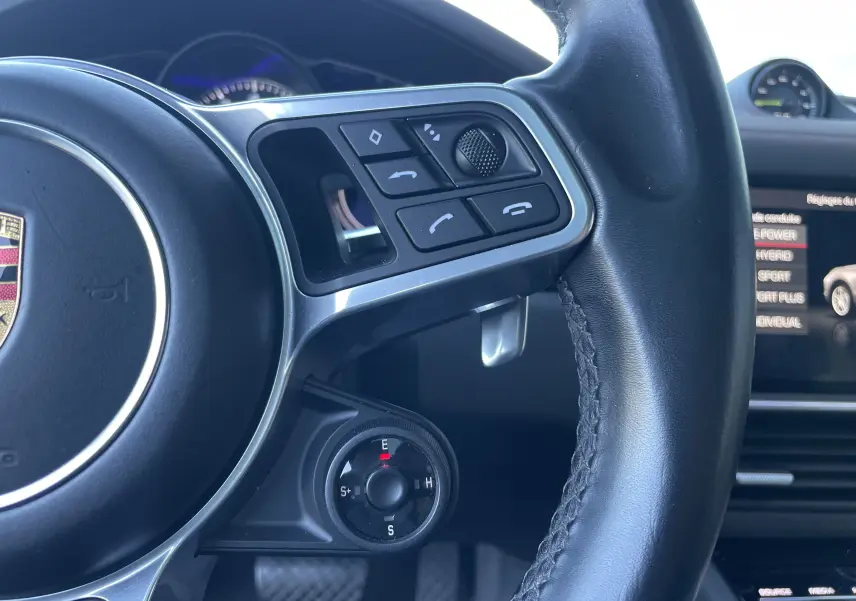 Gros plan sur le volant cuir noir du Porsche Cayenne Coupé e-Hybrid avec commandes multifonctions et sélecteur de mode de conduite.