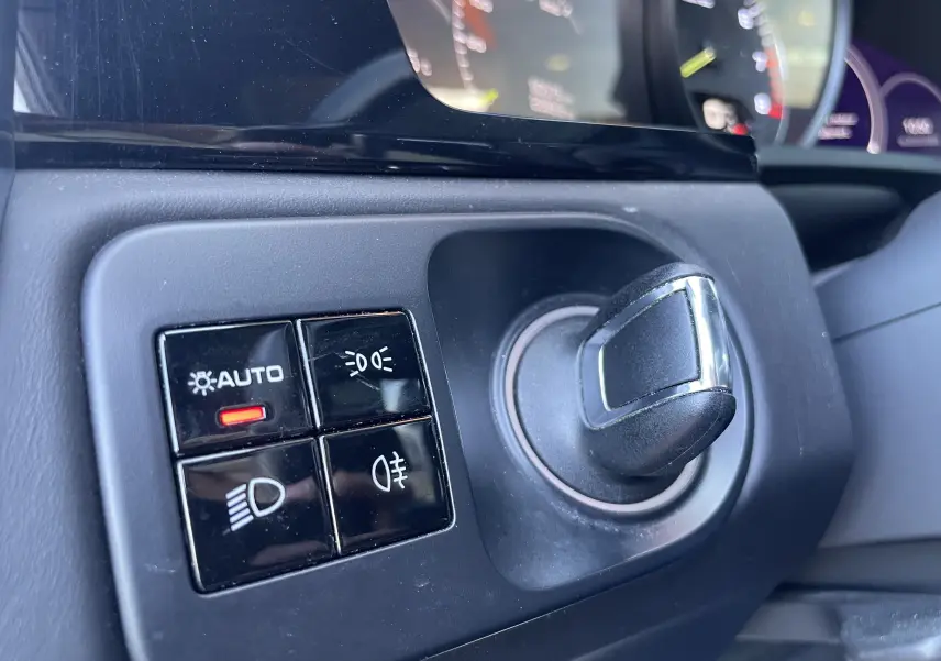 Gros plan sur le sélecteur de phares noir et chrome du tableau de bord intérieur d’un Porsche Cayenne Coupé e-Hybrid 2021.