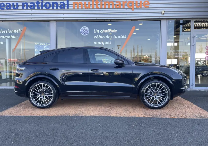 Vue de profil côté gauche d’un Porsche Cayenne Coupé E-Hybrid noir avec jantes alliage 22 pouces devant un showroom.