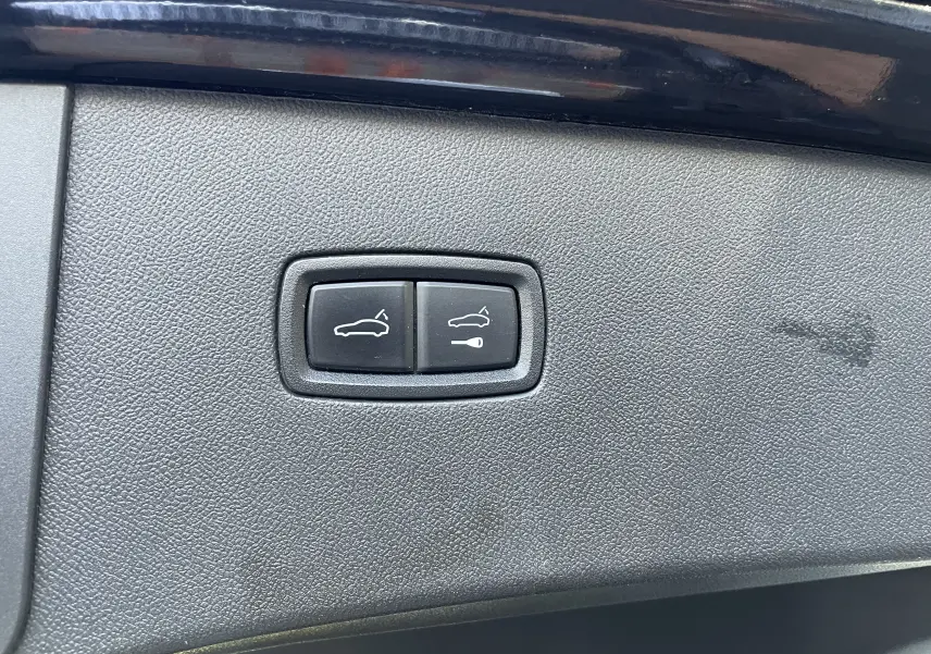Gros plan sur les boutons d'ouverture du coffre et du hayon électrique sur un Porsche Cayenne Coupé noir.