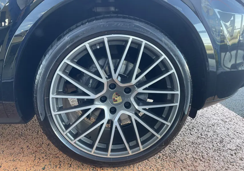 Gros plan sur la jante alu 22 pouces à rayons multiples du côté avant droit du Porsche Cayenne Coupé E-Hybrid noir.