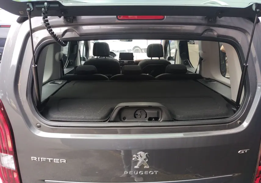 Vue arrière du Peugeot Rifter gris platinium 2022 avec hayon ouvert, montrant l'intérieur et la tablette de coffre.