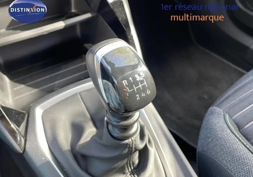 Gros plan sur le levier de vitesses manuel noir du Peugeot 2008 2024, avec siège tissu gris et surpiqûres vertes visibles.