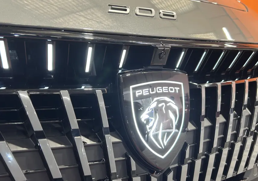 Gros plan sur la calandre noire brillante et le logo lumineux du lion Peugeot sur une 308 gris Selenium.