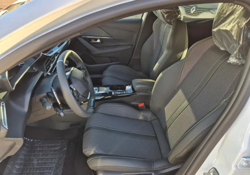 Intérieur avant droit de la Peugeot 208 Hybrid 136 e-DCS6 GT blanc 2025, sièges noirs avec surpiqûres vertes et volant multifonction.