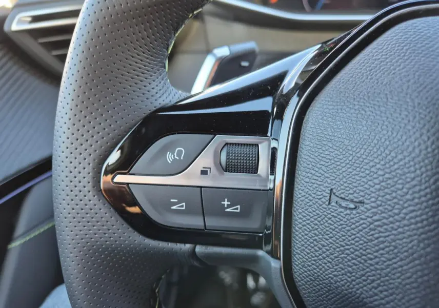 Gros plan sur le volant noir perforé du Peugeot 208 Hybrid 136 e-DCS6 GT avec commandes intégrées côté gauche.