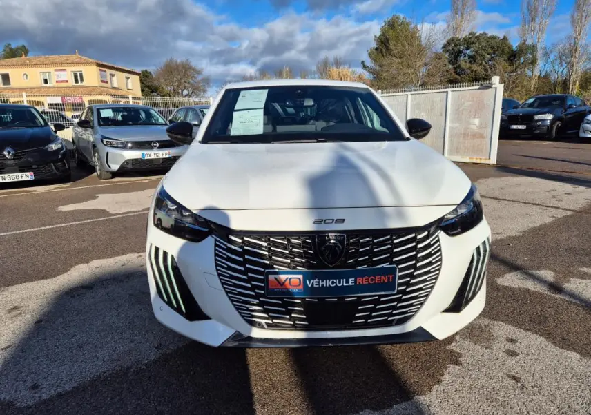 Vue de face d'une Peugeot 208 Hybrid 136 e-DCS6 GT blanche avec calandre noire et feux LED diurnes distinctifs.