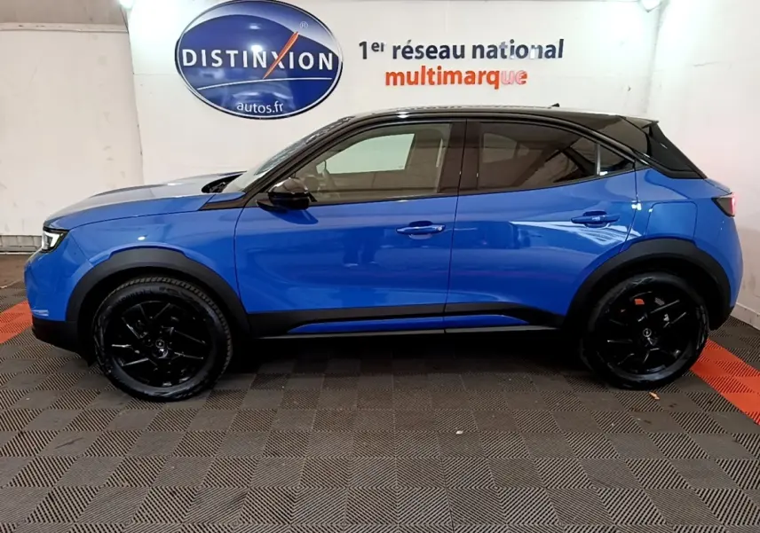 Vue latérale droite d'un Opel Mokka 2024 bleu avec toit noir et jantes noires dans un showroom.