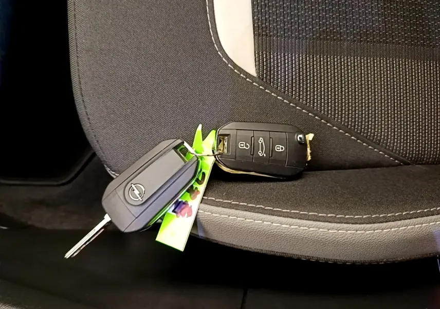 Gros plan sur deux clés Opel posées sur un siège tissu noir avec surpiqûres blanches, intérieur du véhicule visible.