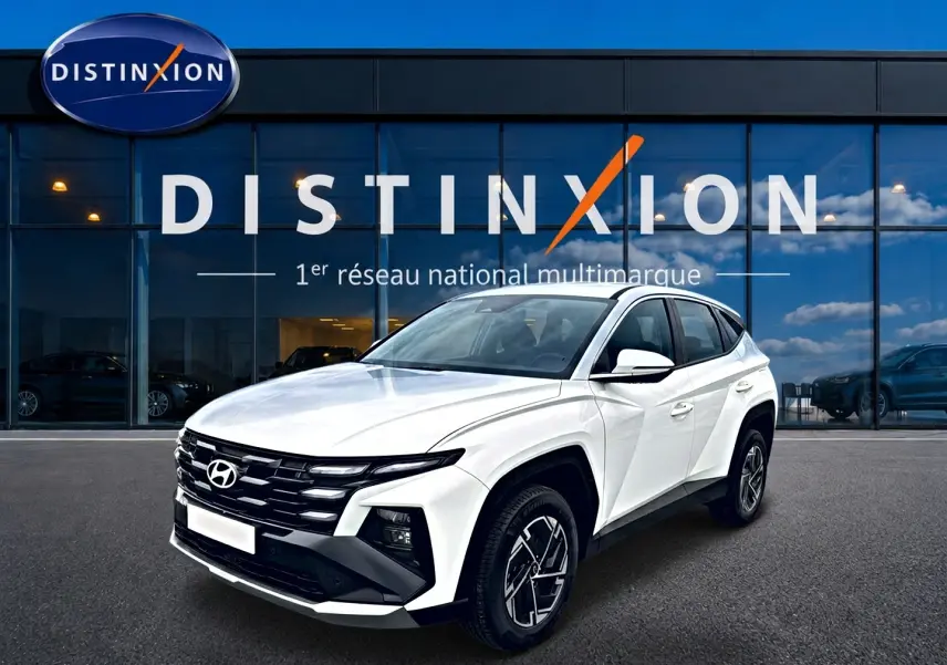 Vue 3/4 avant d'un Hyundai Tucson blanc 2026 devant une vitrine avec logo Distinxion.