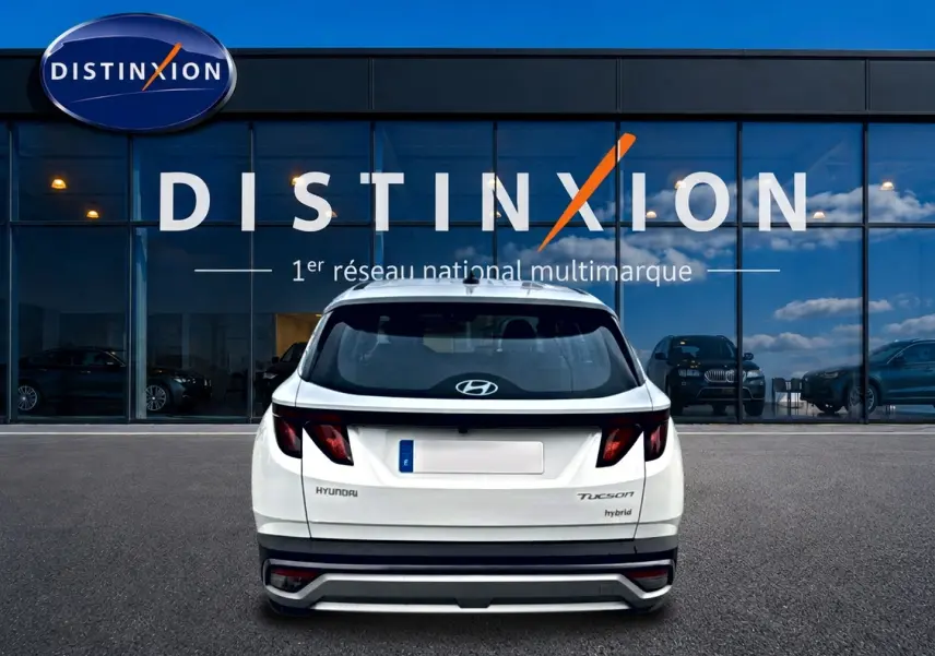 Vue arrière d'un Hyundai Tucson blanc hybride 2026 garé devant une vitrine avec logo Distinxion.