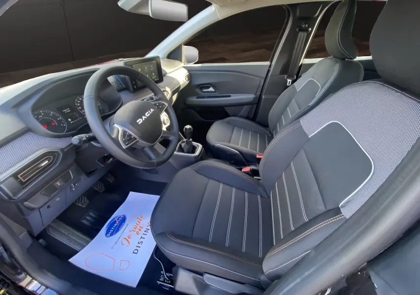 Vue intérieure côté conducteur de la Dacia Sandero Stepway 2025 avec sièges tissu noir et tableau de bord moderne.