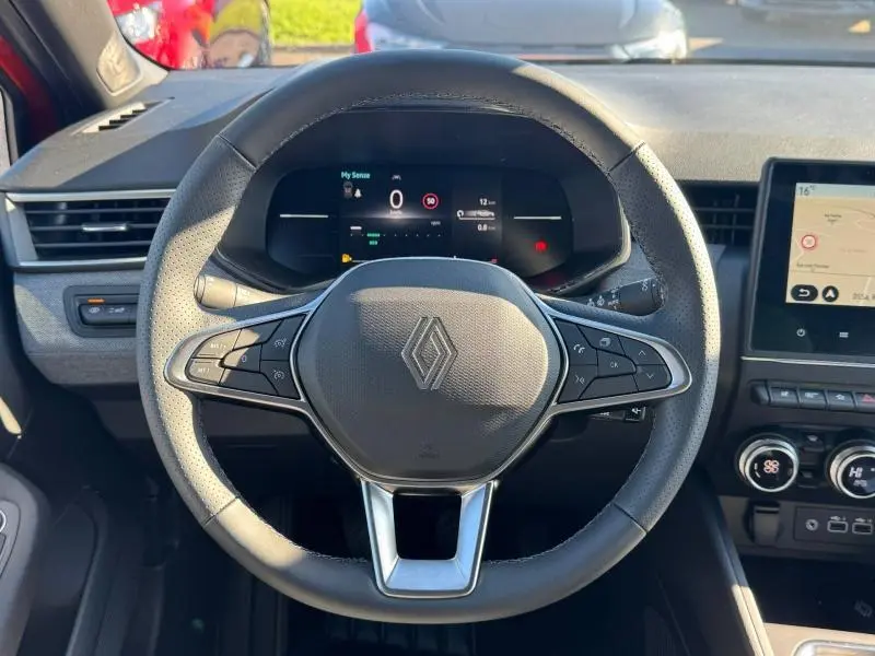 Vue intérieure centrée sur le volant cuir multifonction de la Renault Clio orange 2025 avec tableau de bord numérique et écran tactile.