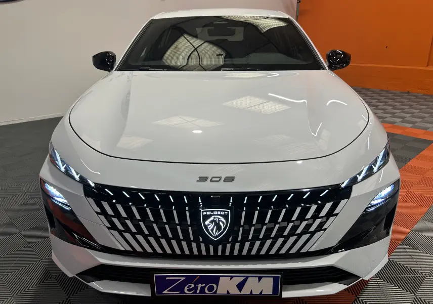 Vue frontale d’une Peugeot 308 blanche Okenite avec calandre noire et logo lumineux au centre.