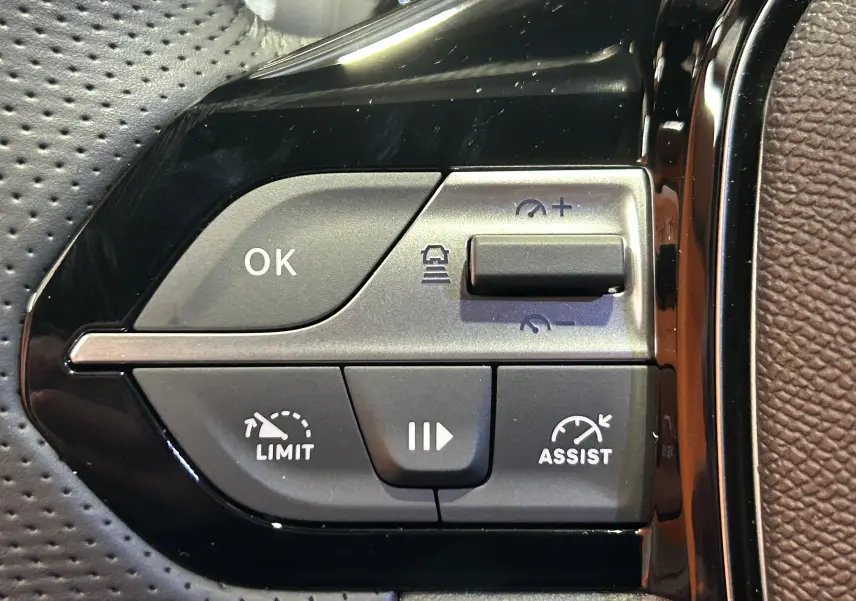 Gros plan sur les commandes de régulateur de vitesse et assistance au volant d’une Peugeot 308 blanc Okenite.