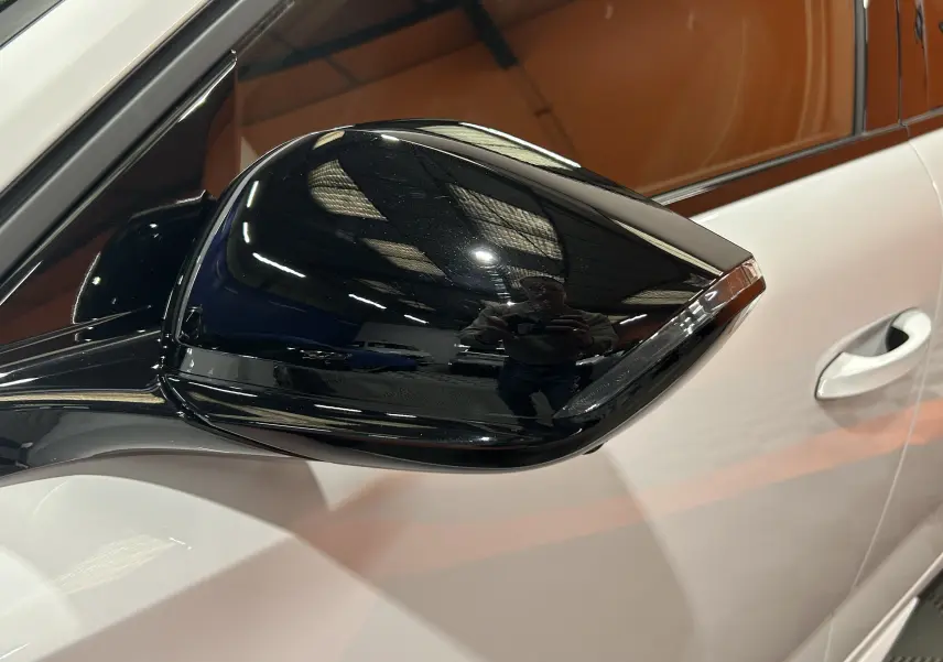 Gros plan sur le rétroviseur noir brillant côté gauche d'une Peugeot 308 blanche Okenite, avec reflet intérieur visible.