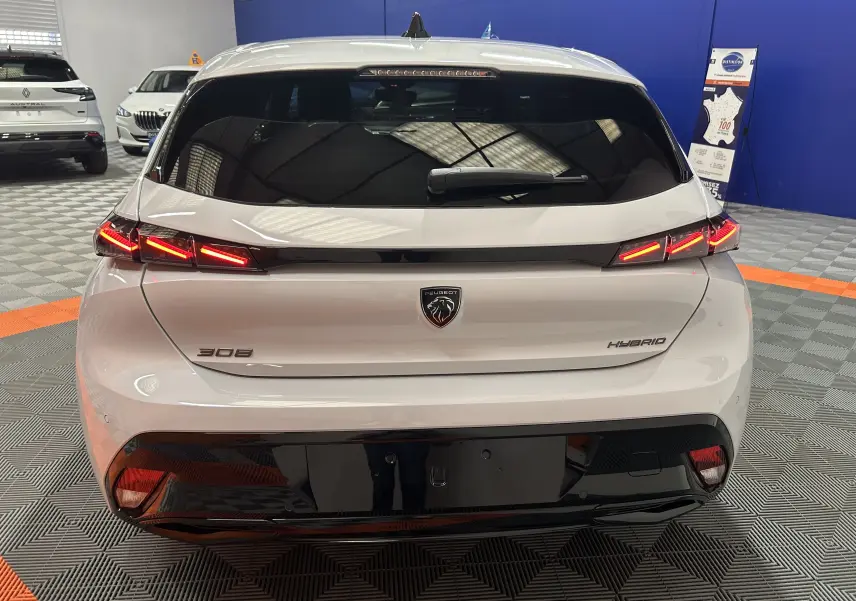 Vue arrière d'une Peugeot 308 blanche Okenite hybride avec feux arrière LED allumés dans un showroom.