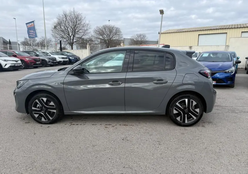Profil droit d'une Peugeot 208 gris 2025 avec jantes alliage et antenne requin sur parking extérieur.