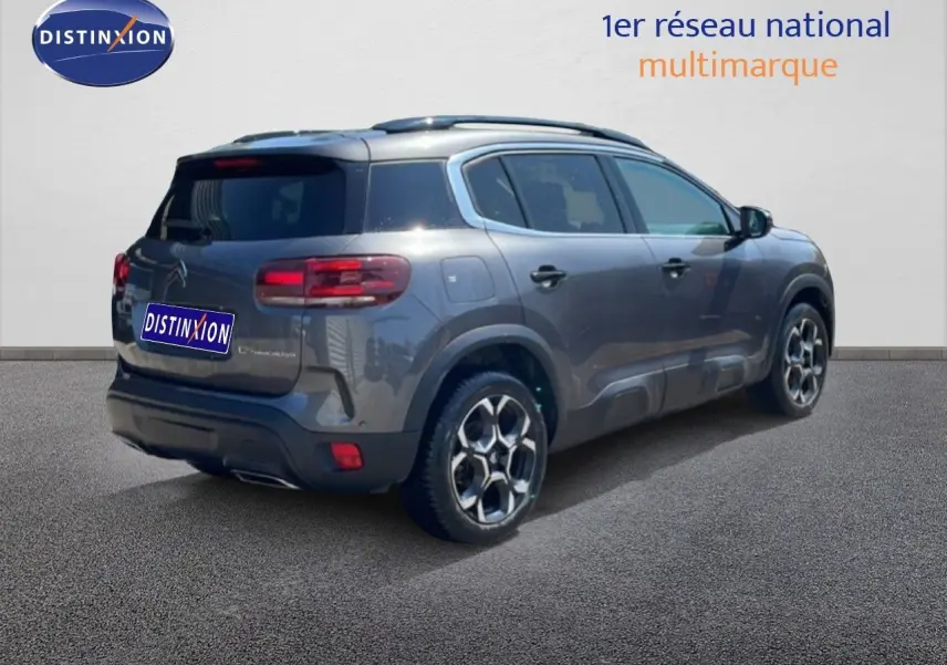 Vue 3/4 arrière droite d'un Citroën C5 Aircross gris platinium métallisé avec jantes bi-ton et barres de toit.