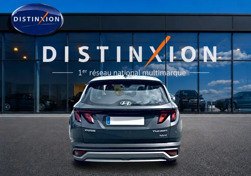 Vue arrière d'un Hyundai Tucson hybride gris ecotronique garé devant une vitrine avec logo Distinxion.