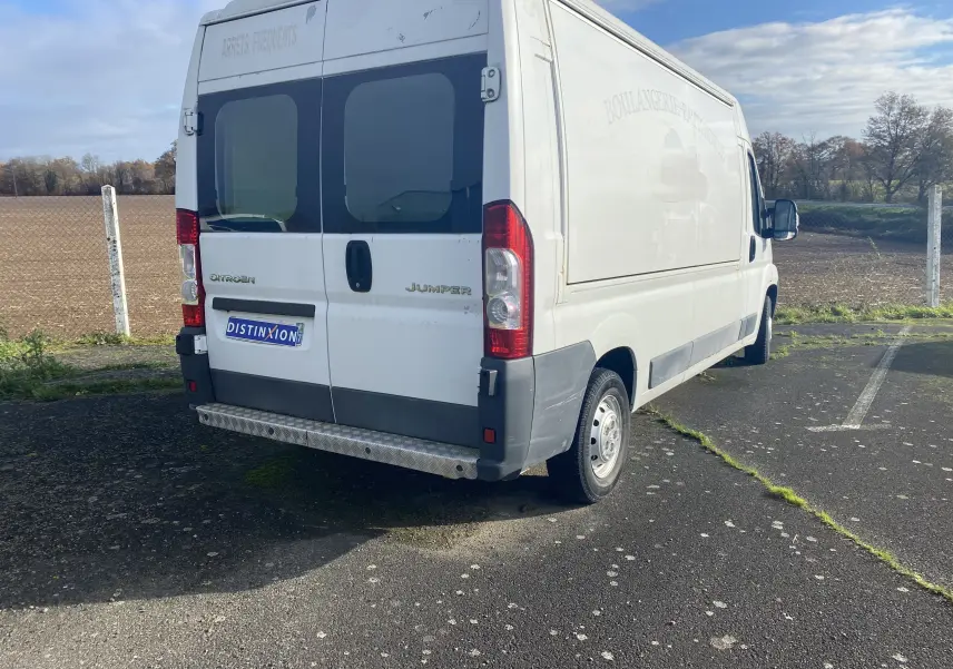 Vue 3/4 arrière droite d'un utilitaire Citroën Jumper blanc avec portes arrière vitrées et marquage publicitaire effacé.
