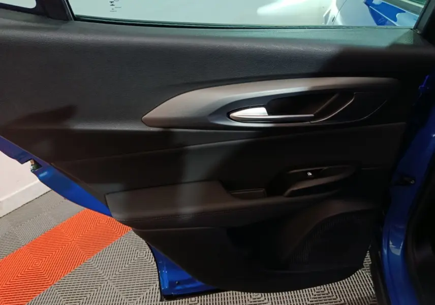 Vue intérieure côté gauche de la porte avant bleu de l'Alfa Romeo Tonale avec poignée argentée et commande de verrouillage.