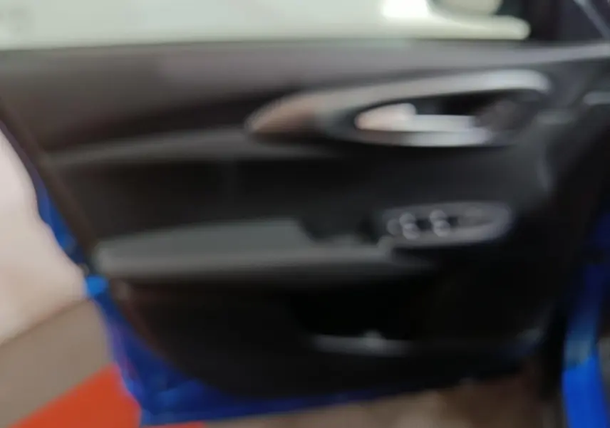 Vue intérieure de la porte avant gauche d'une Alfa Romeo Tonale bleu, avec poignée et commandes de vitres visibles.