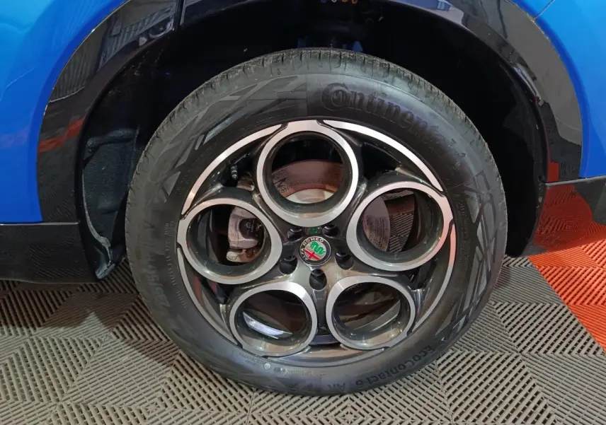 Gros plan sur la roue avant droite bleue d'une Alfa Romeo Tonale 1.3T PHEV avec jante distinctive à cinq cercles.