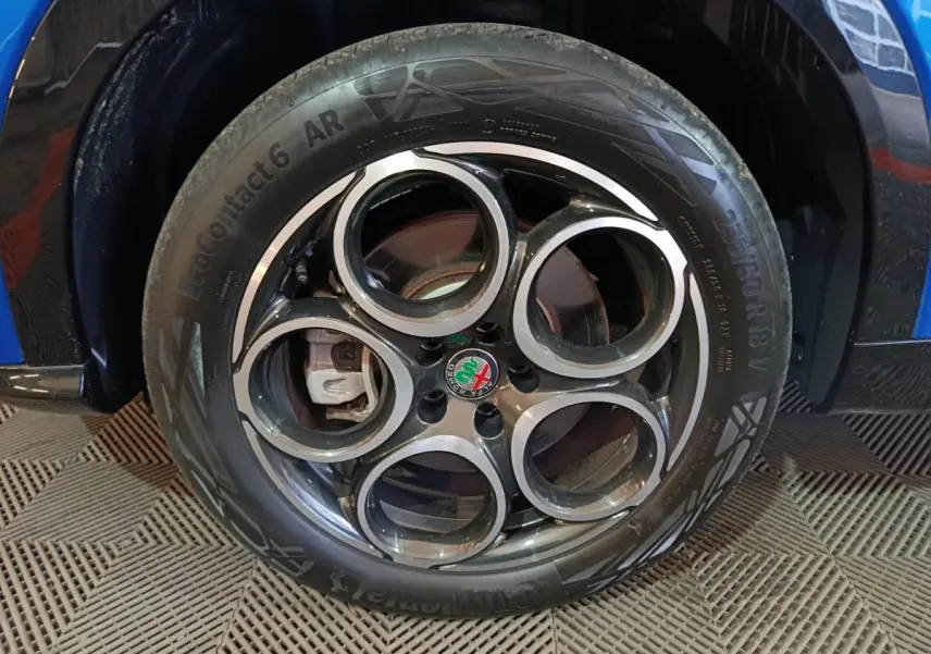 Gros plan sur la roue avant droite bleue d'une Alfa Romeo Tonale avec jante en alliage à cinq cercles distinctifs.