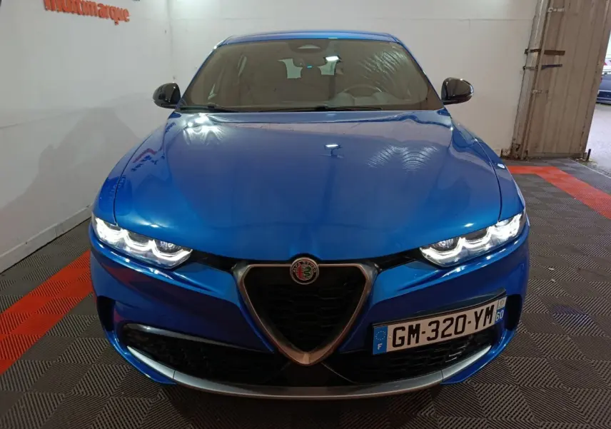 Vue avant d'une Alfa Romeo Tonale bleu électrique avec phares allumés et calandre caractéristique en V.