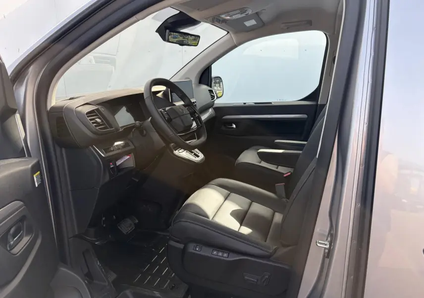 Vue intérieure côté conducteur du Citroën Jumpy gris acier, montrant sièges cuir et tableau de bord moderne.