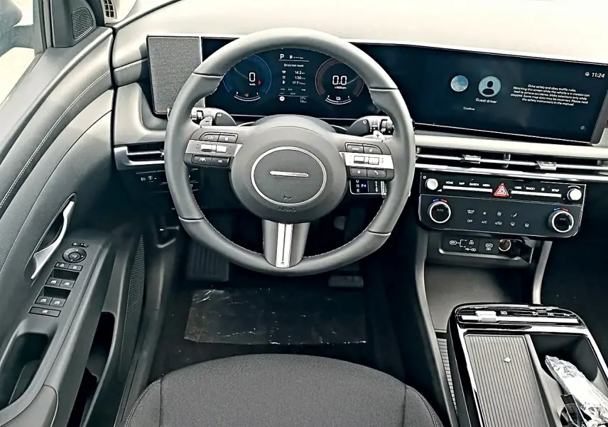 Vue intérieure frontale du tableau de bord gris du Hyundai Tucson 2026 avec volant cuir multifonction et écran digital large.