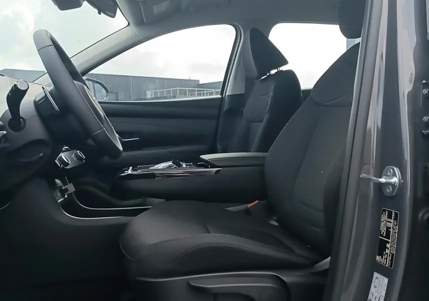 Vue intérieure côté gauche du Hyundai Tucson gris ecotronique 2026, mettant en valeur les sièges avant et l'accoudoir central.