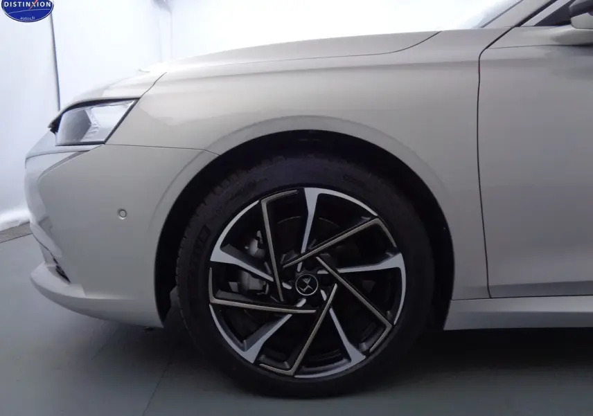 Gros plan sur la roue avant gauche de la DS9 hybride en Crystal Pearl nacré, soulignant la jante noire et argentée au design moderne.