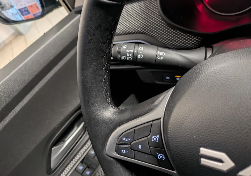 Gros plan sur le volant noir du Dacia Jogger 2025, avec commandes de régulateur de vitesse et manette d’éclairage visible.