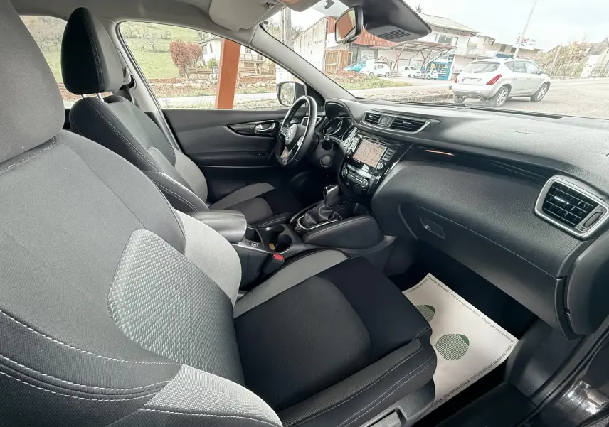 Vue intérieure côté passager du Nissan Qashqai 2020 noir, montrant sièges tissu bicolore et tableau de bord avec écran tactile.