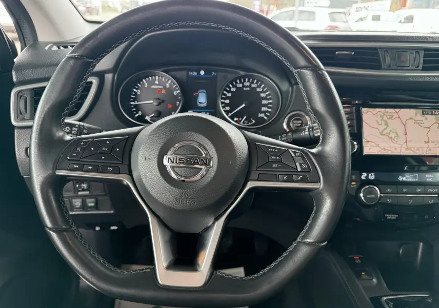 Vue intérieure centrée sur le volant cuir noir du Nissan Qashqai avec tableau de bord et écran GPS visible.