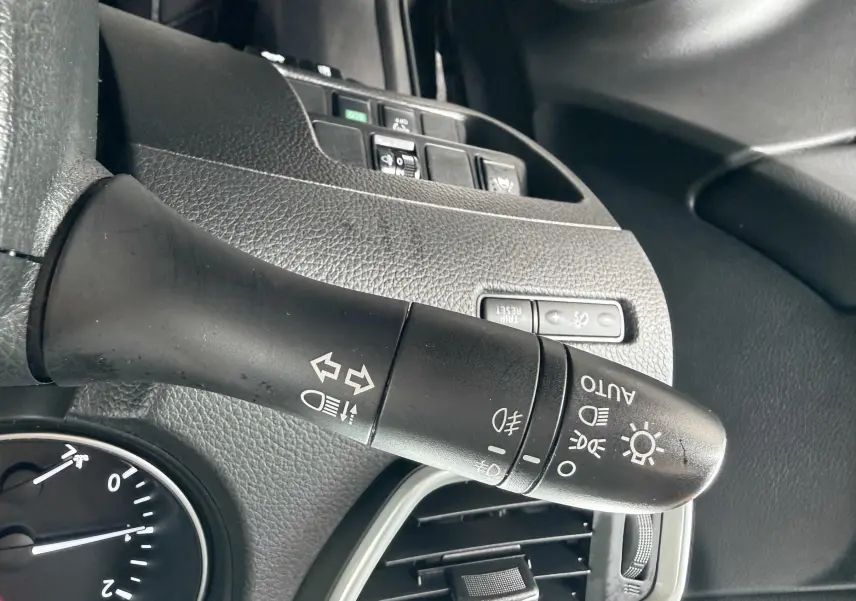 Gros plan sur la manette de commandes d’éclairage noire à gauche du volant dans l’habitacle d’un Nissan Qashqai noir.