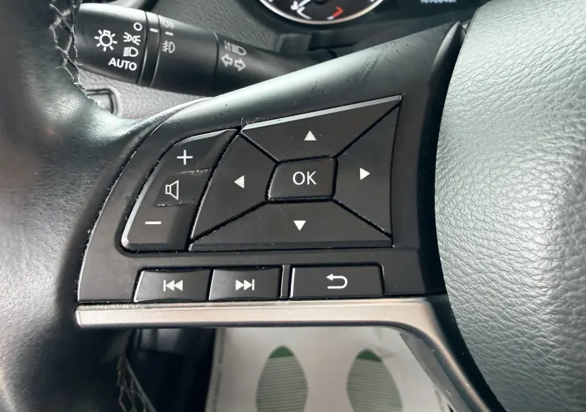 Gros plan sur les commandes gauche du volant noir du Nissan Qashqai 2020, avec boutons de navigation et volume.