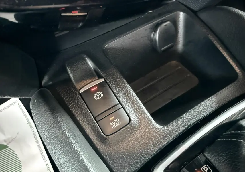 Gros plan sur la console centrale du Nissan Qashqai noir, montrant les boutons frein à main électrique et auto hold.