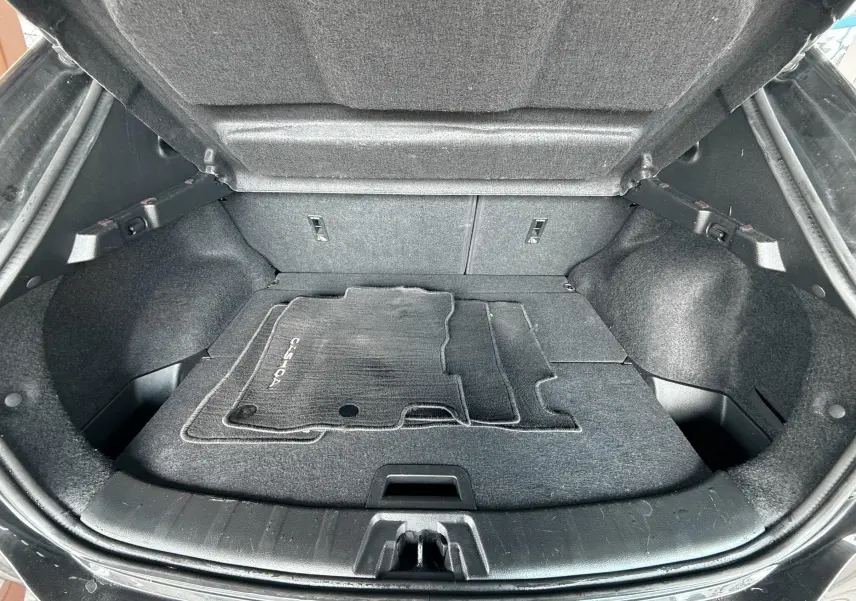 Coffre ouvert vu de l'arrière d'un Nissan Qashqai noir avec tapis de sol noir à l'intérieur.