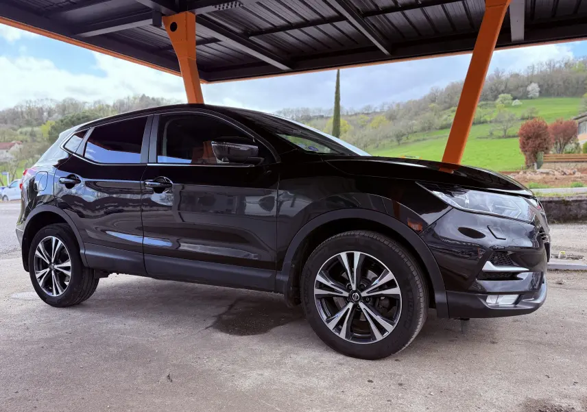 SUV Nissan Qashqai noir vu de profil côté gauche sous un abri avec jantes alliage bicolores.